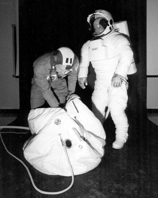 Двоє астронавтів у скафандрах демонструють, як потрапити в тканинну рятувальну кулю.
