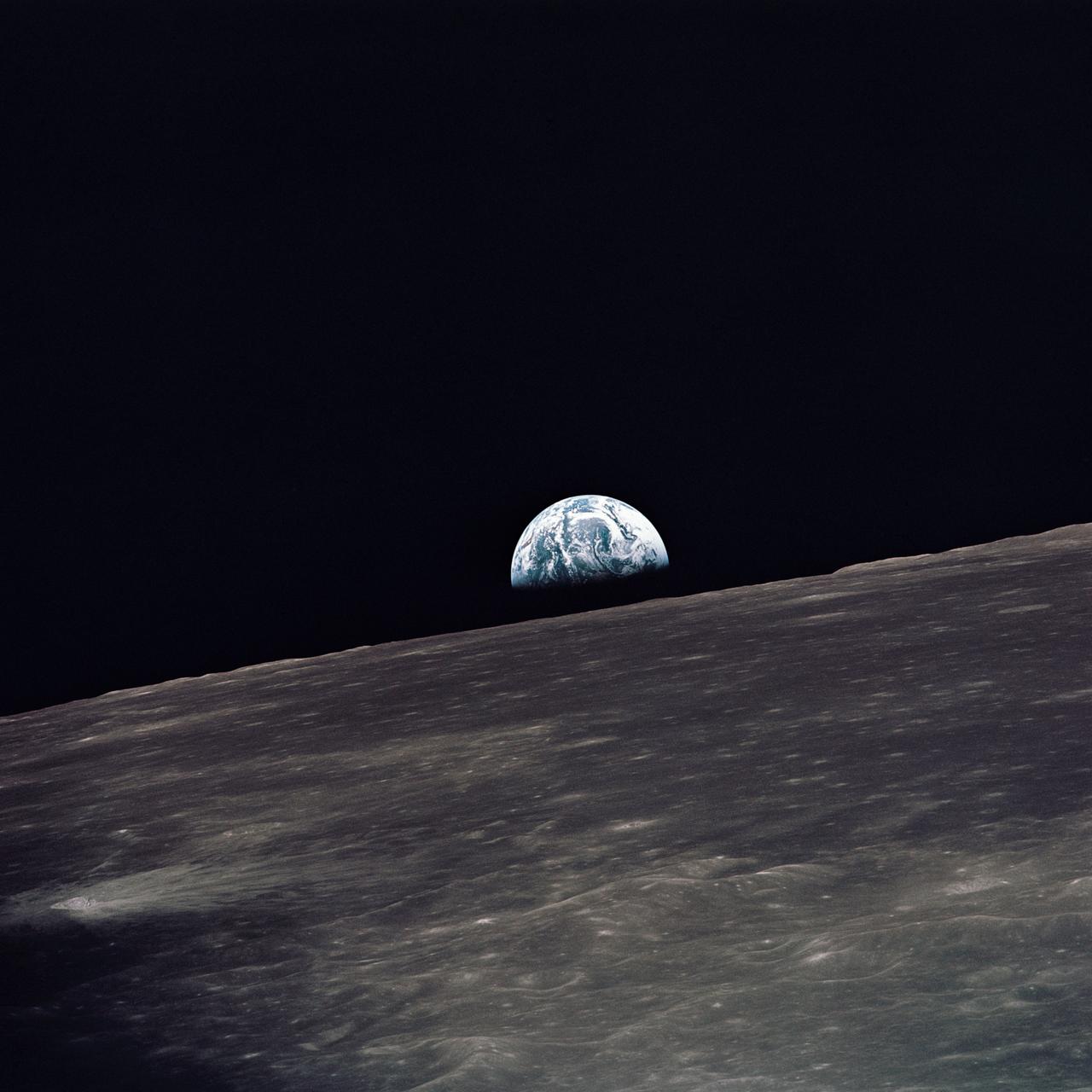 Вид на Землю, що піднімається над місячним горизонтом, сфотографований з місячного модуля «Аполлон-10», дивлячись на захід у напрямку руху.  Місячний модуль у момент, коли було зроблено знімок, знаходився над нагір’ям зворотного боку Місяця приблизно на 105 градусах східної довготи.